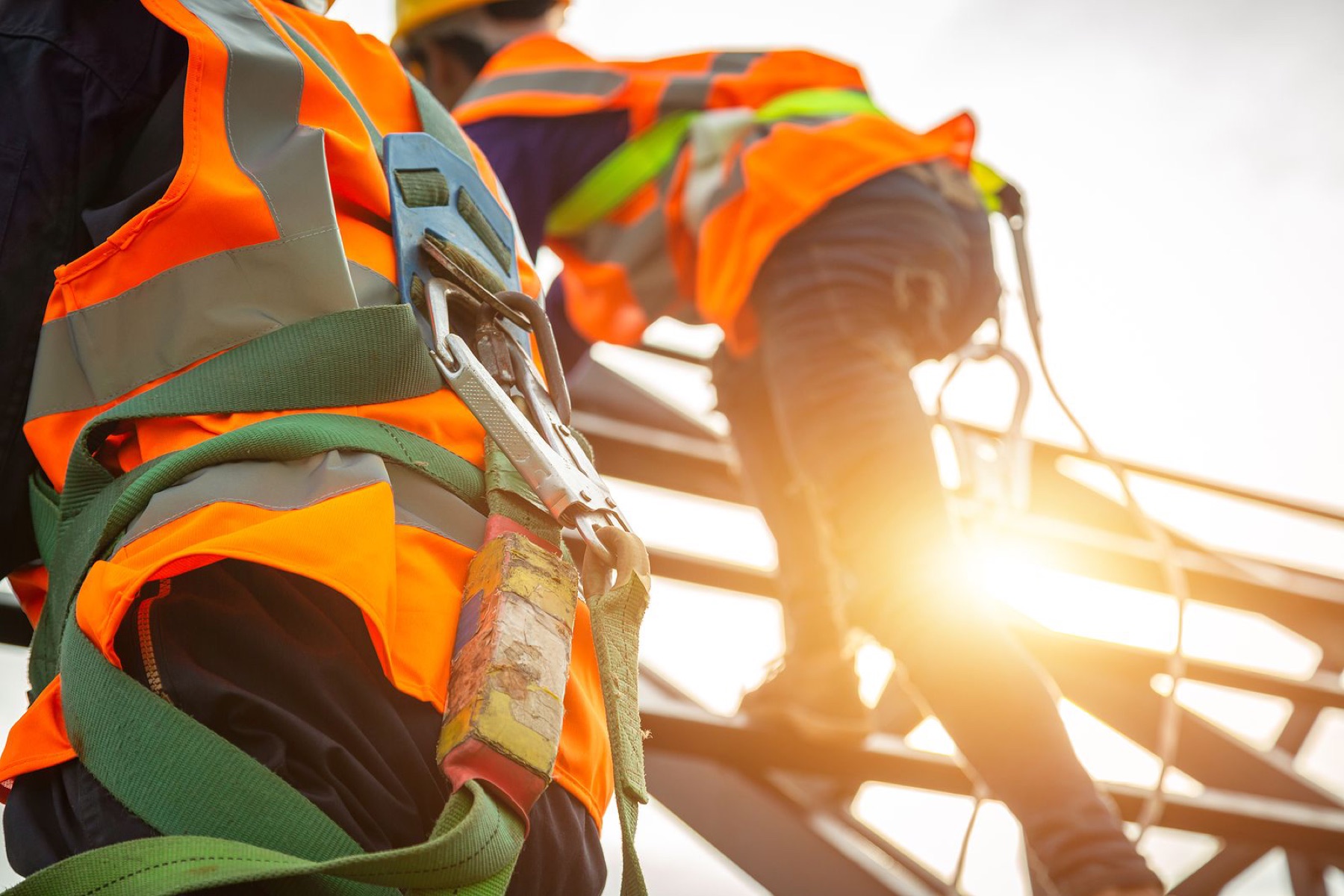 Workers in harnesses and hi-vis vests climbing a steel structure